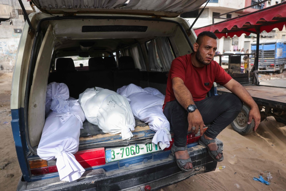 A Palestinian man sits by shrouded bodies killed in Israeli strikes, in the back of a van outside Al-Shifa hospital in Gaza City on May 18, 2025. (Photo by Bashar TALEB / AFP)
