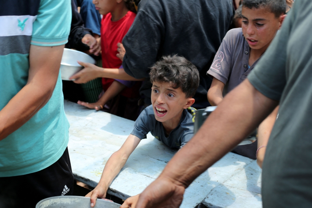 Palestinians gather for a hot meal at a food distribution point in the Nuseirat camp for refugees in the central Gaza Strip on May 21, 2025. (Photo by Eyad Baba / AFP)