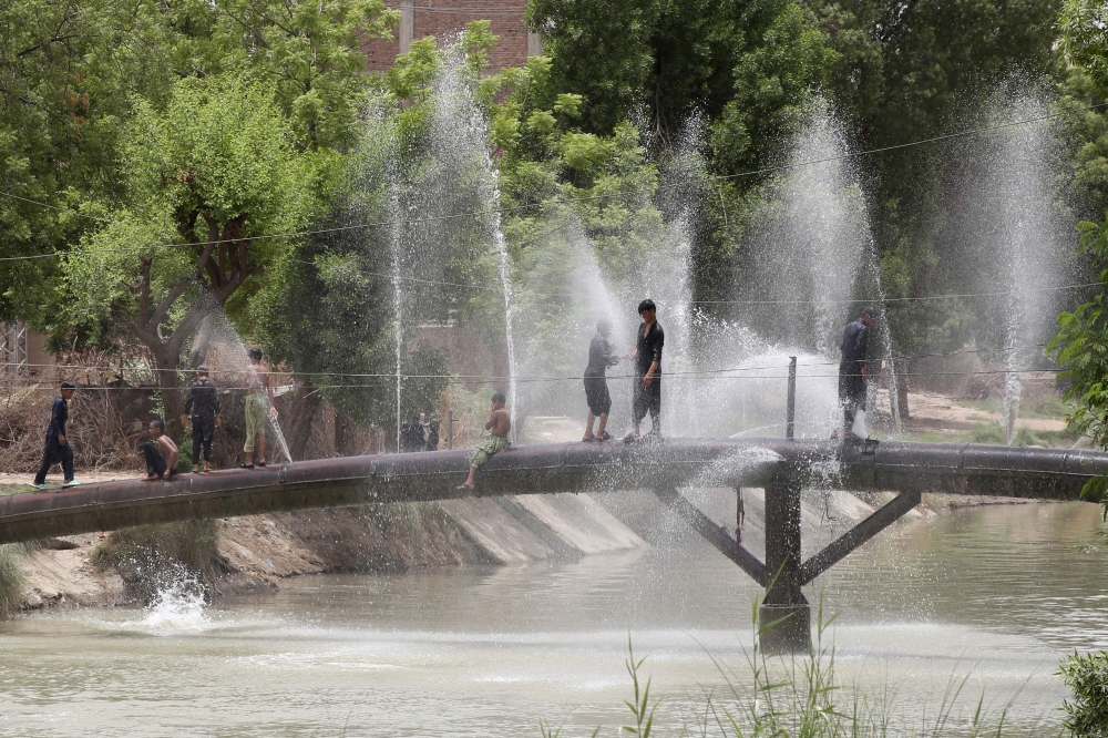 Young boys cool off over a leaking water supply pipeline on a hot summer day in Hyderabad, a town of Sindh Province, on May 27, 2025. (Photo by Akram Shahid / AFP)
 