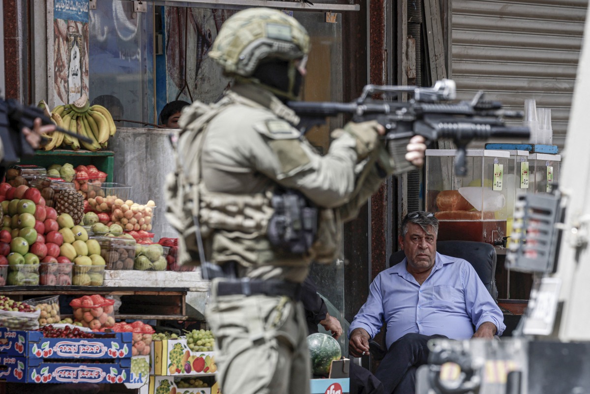 Photo used for representational purposes. An Israeli occupation soldier aims his rifle as a Palestinian man looks on during a raid in the heart of the Palestinian city of Nablus, in the occupied West Bank on May 27, 2025. Photo by Jaafar ASHTIYEH / AFP.