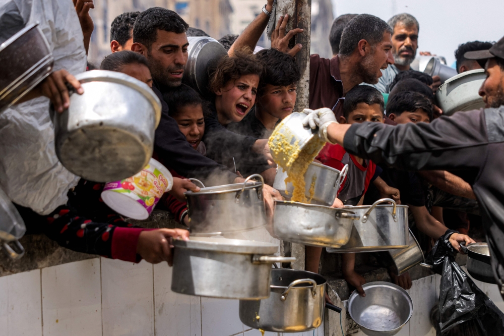 People queue with pots to receive charity meals from a kitchen in Beit Lahia in the northern Gaza Strip on April 24, 2025. (Photo by Bashar Taleb / AFP)