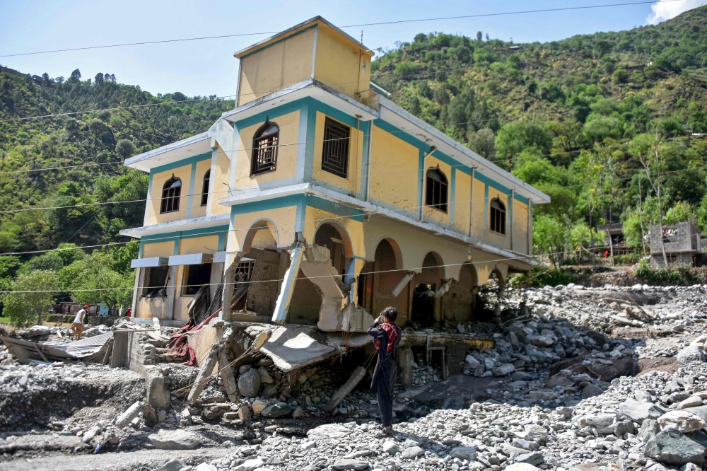 A man takes pictures of a damaged mosque, a day after flash floods in Balgran village near Muzaffarabad, capital of Pakistan-administered Kashmir on May 28, 2025. (Photo by Sajjad Qayyum / AFP)