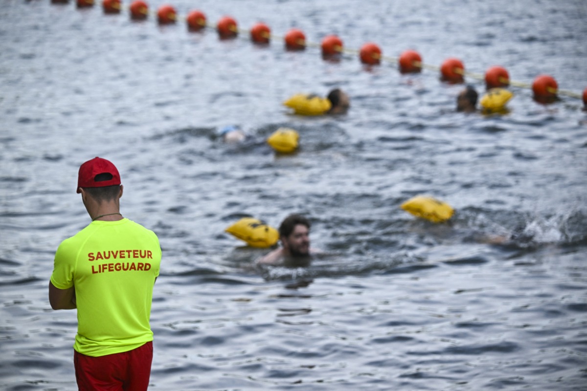 A lifeguard stands on duty as people swim at the Pont Marie safe bathing site on the Seine river on its opening day, in Paris on July 5, 2025. Photo by JULIEN DE ROSA / AFP.
