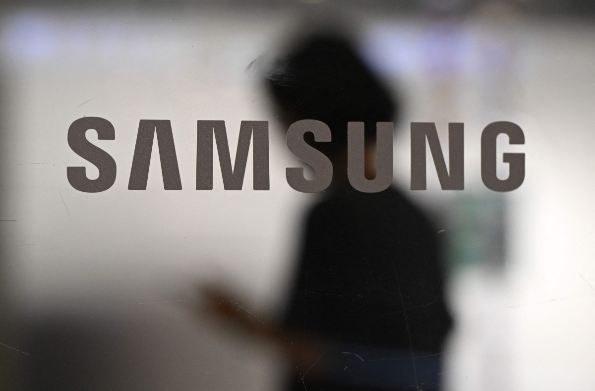 A woman walks past a logo of Samsung Electronics displayed on a glass door at the company's Seocho building in Seoul on July 8, 2025. Photo by Jung Yeon-je / AFP