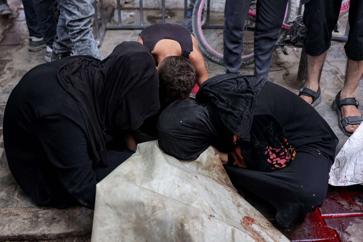 Women and a boy mourn by the body of a victim killed by gunfire while waiting for aid trucks entering the northern Gaza Strip through the Zikim crossing, as it lays on the ground at the Shifa Hospital in Gaza City on July 27, 2025. (Photo by Omar AL-QATTAA / AFP)
