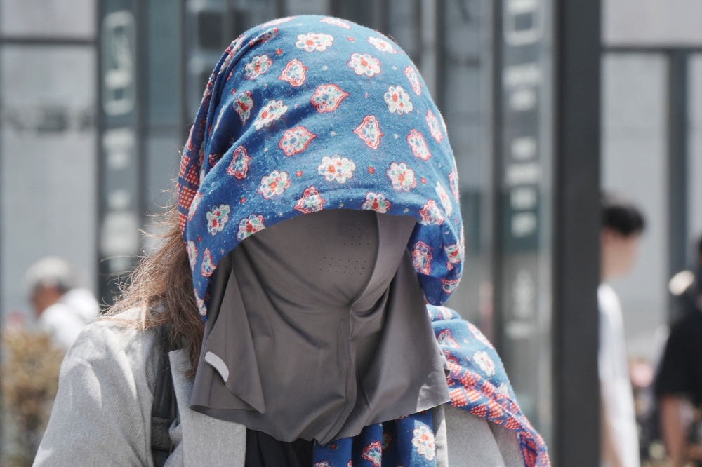 A pedestrian wears a cloth over her head to protect herself from the heat and sun on a hot day in Tokyo on August 5, 2025. (Photo by Kazuhiro Nogi / AFP)