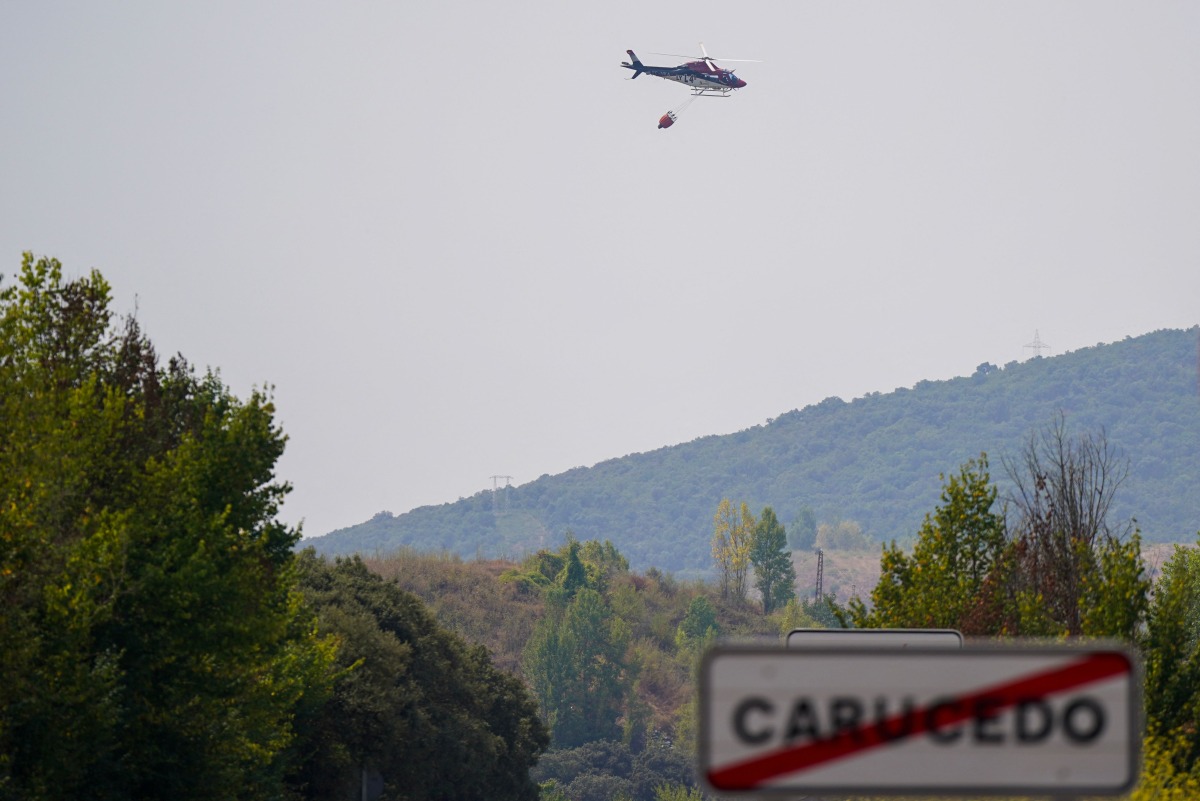 A firefighting helicopter flies with a bucket during a wildfire near the UNESCO World Heritage Site of Las Medulas, a former Roman gold-mining area known for its striking red landscape, in Carucedo, northern Spain on August 11, 2025. Photo by CESAR MANSO / AFP