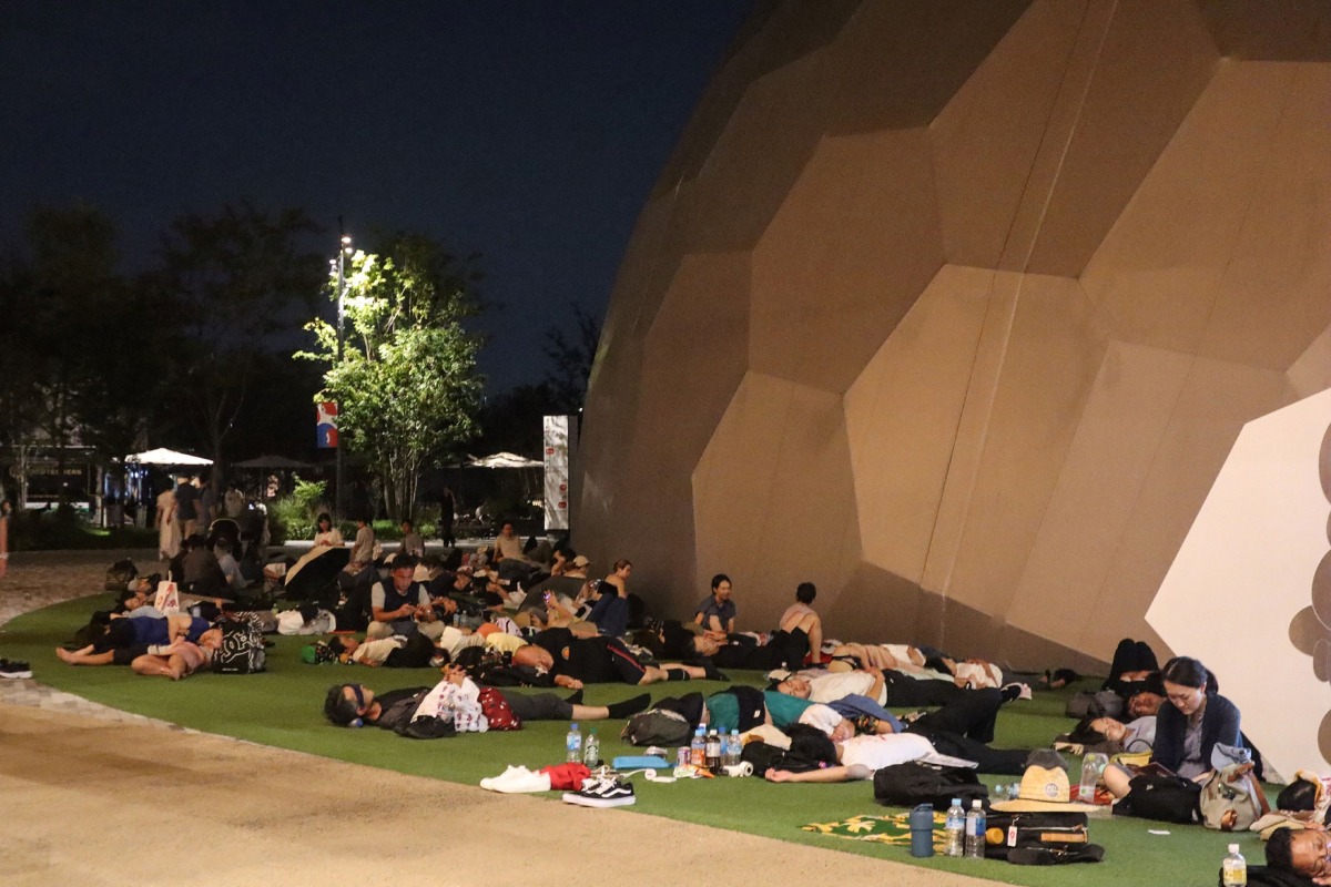 Visitors sleep outside one of the venues overnight after a power outage abruptly shut down the Osaka Metro line linking the city to the 2025 Osaka Expo site, in Osaka early on August 14, 2025. Photo by JIJI Press / AFP