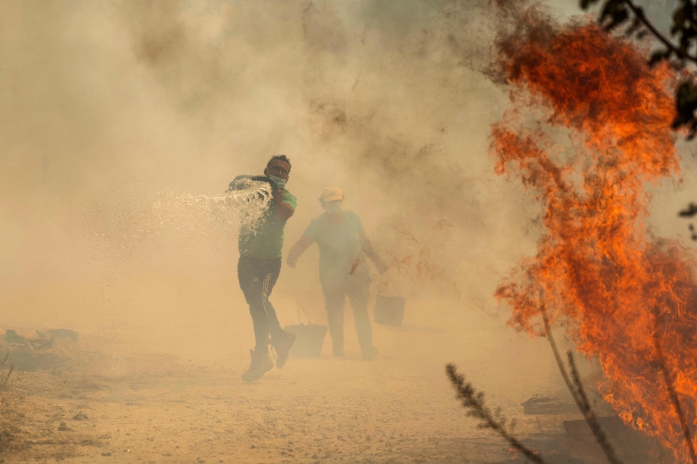 People use buckets of water to extinguish a wildfire that threatens their house in the Portuguese village of Antas, in Trancoso, on August 15, 2025. (Photo by Patricia De Melo Moreira / AFP)