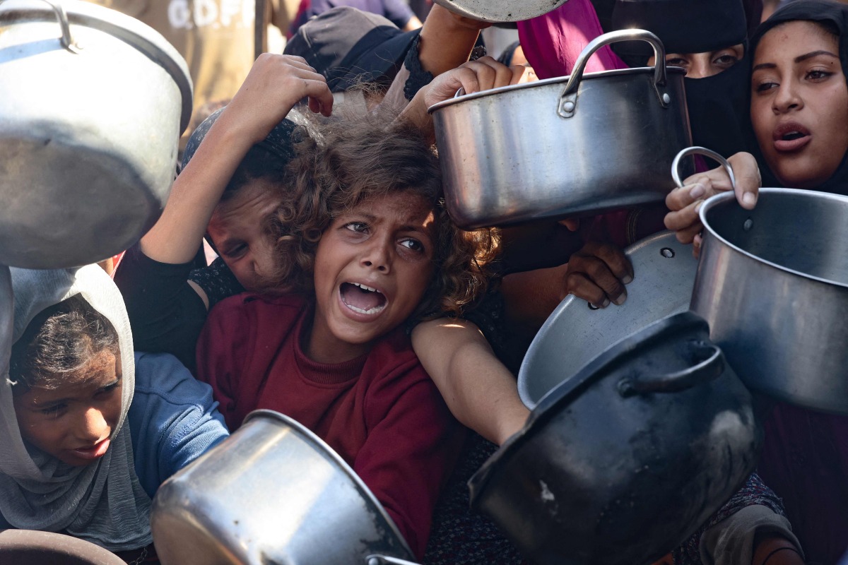 Palestinian women and children hold out their empty pots in front of a charity kitchen in Khan Yunis in the southern Gaza Strip on August 21, 2025. Photo by AFP