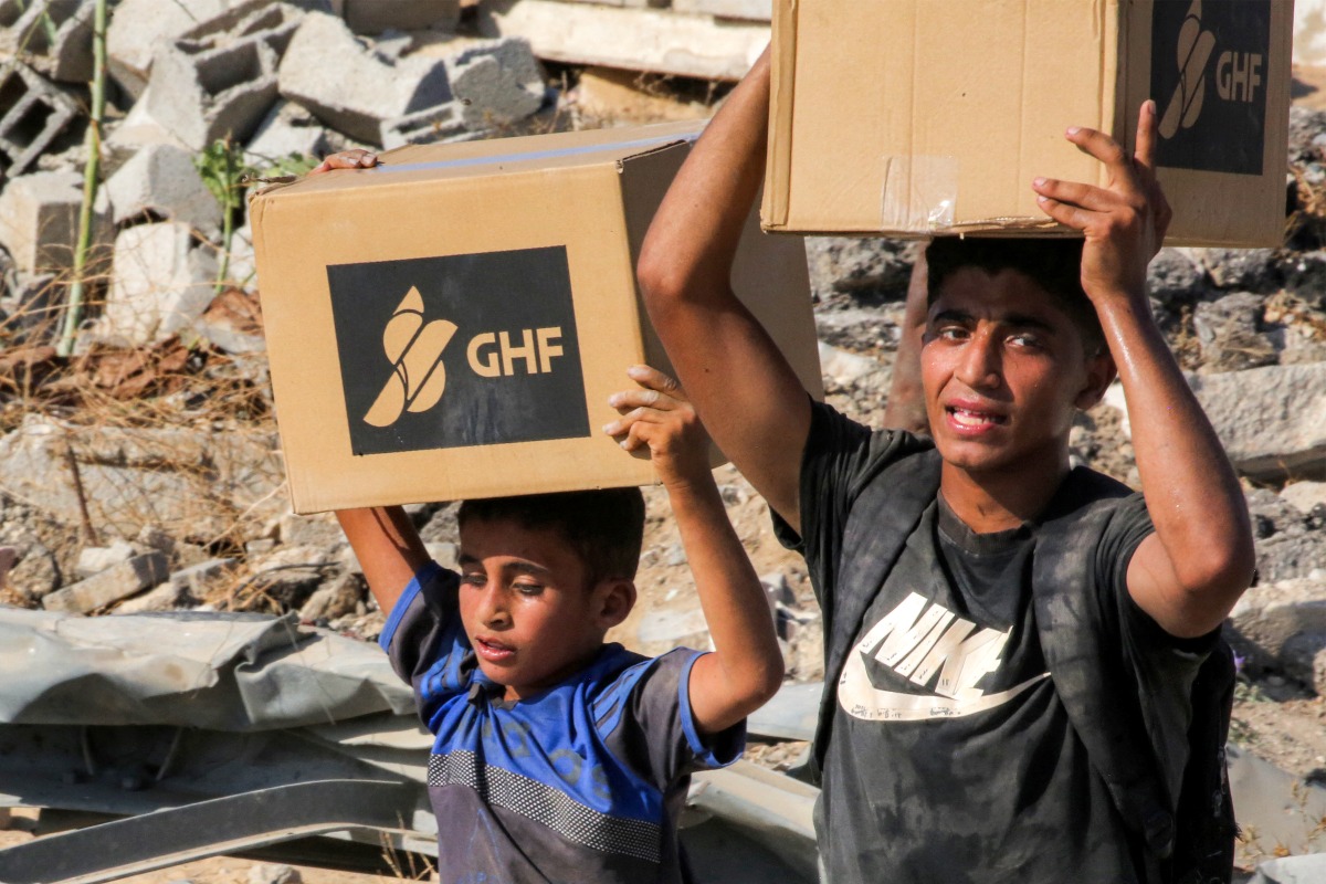 Boys walk with boxes of humanitarian aid they received at a distribution centre run by the US and Israeli-backed Gaza Humanitarian Foundation (GHF), as they cross the so-called 
