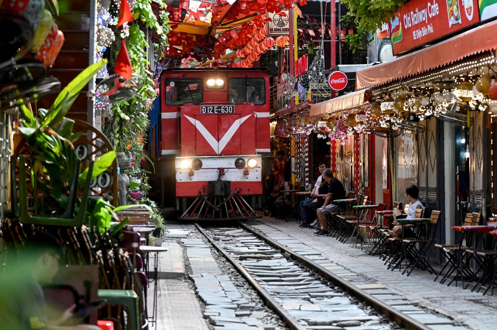 This photo taken on August 18, 2025 shows a train as it passes along a railway track between cafe terraces in central Hanoi. (Photo by Nhac Nguyen / AFP)