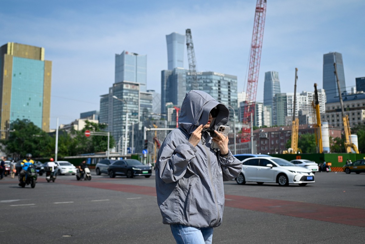 A woman wearing sun protective clothing crosses a street in Beijing on June 23, 2025. Photo by WANG Zhao / AFP