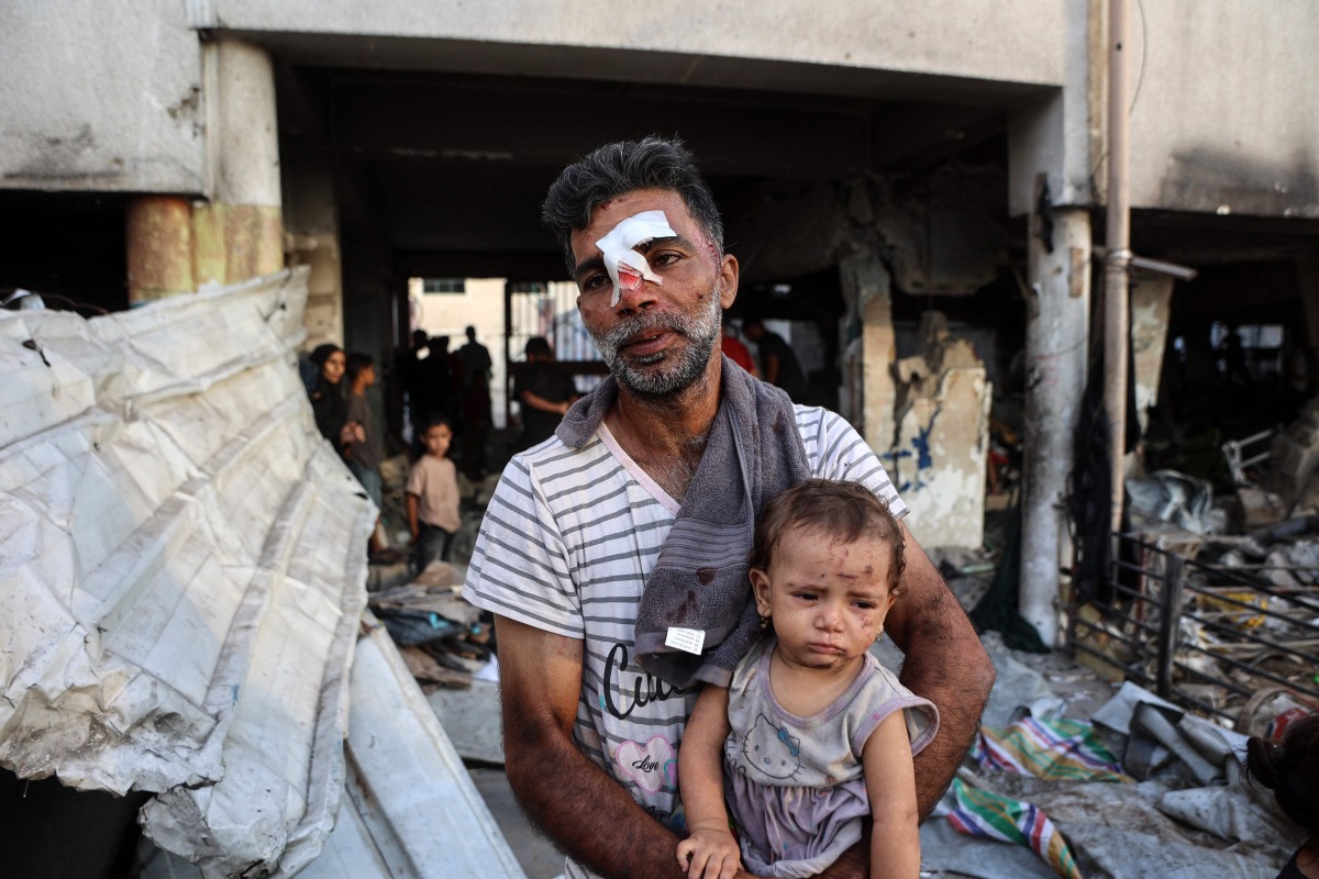 An injured man carries a toddler as others search for their belongings amid the rubble, in the al-Farabi school turned shelter for displaced Palestinians, after it was hit by an Israeli strike, in Gaza City in the northern Gaza Strip on September 7, 2025. (Photo by Omar AL-QATTAA / AFP)