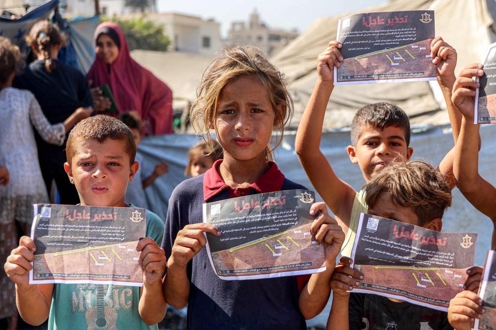 Children hold some of the leaflets dropped by the Israeli military, urging evacuation to al-Mawasi in the southern Gaza Strip, as occupation forces step attacks, on September 12, 2025. (Photo by Omar Al-Qattaa / AFP)