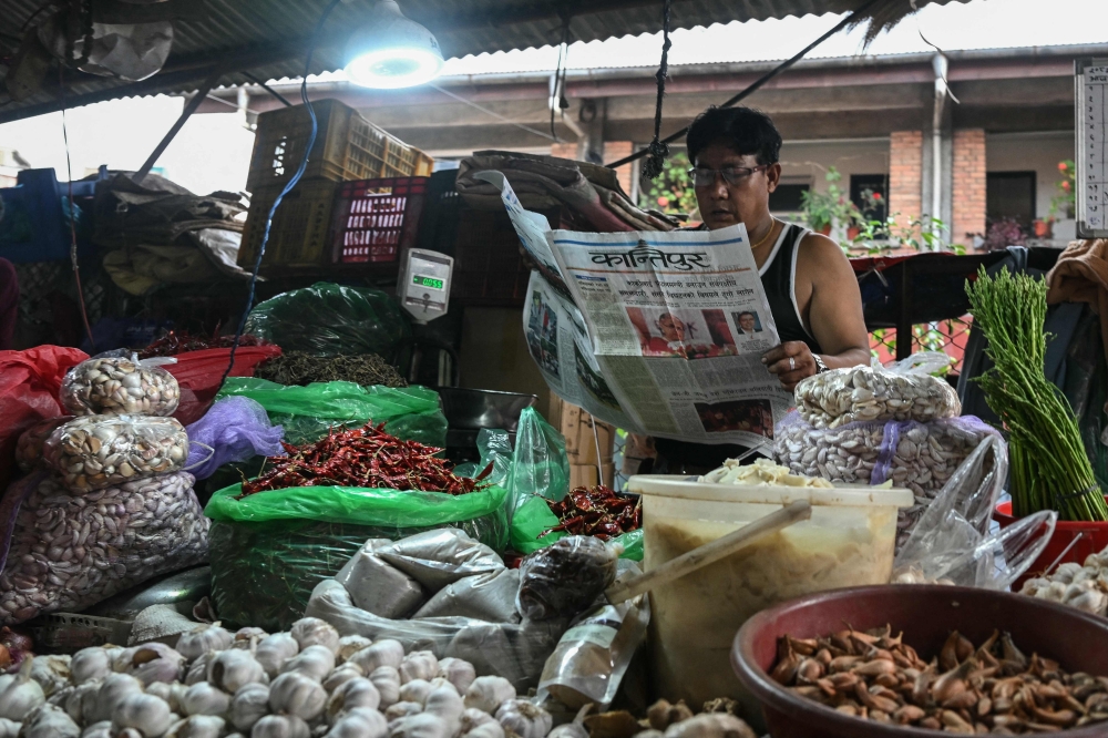 A vegetable vendor reads a Nepali-language newspaper on a roadside in Kathmandu on September 12, 2025. (Photo by Arun Sankar / AFP)
 