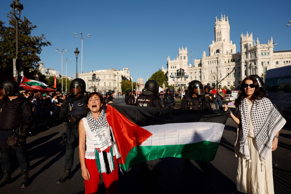 Two women hold a Palestinian flag after Pro-Palestinian protesters invaded the street during the 21st and last stage of the Vuelta a Espana 2025, a 101 km race near Cibeles fountain in Madrid on September 14, 2025.  (Photo by Oscar Del Pozo / AFP)