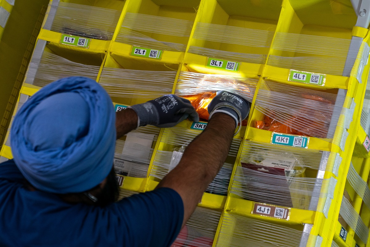 A worker grabs products from a bin at Amazon Fulfillment Center SCK6 in Tracy, California. Photo credit: Jungho Kim/For The Washington Post
