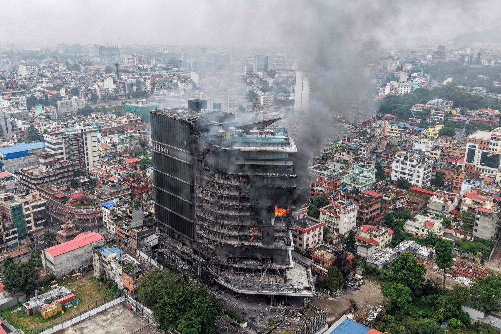 Smoke billows from the burning Hilton Hotels, a day after it was set ablaze by protesters in Kathmandu on September 10, 2025. (Photo by Prabin Ranabhat / AFP)

