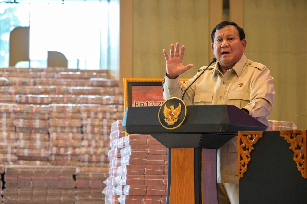 Indonesian President Prabowo Subianto speaks beside stacks of banknotes on October 20, 2025. Photo by Bay Ismoyo / AFP