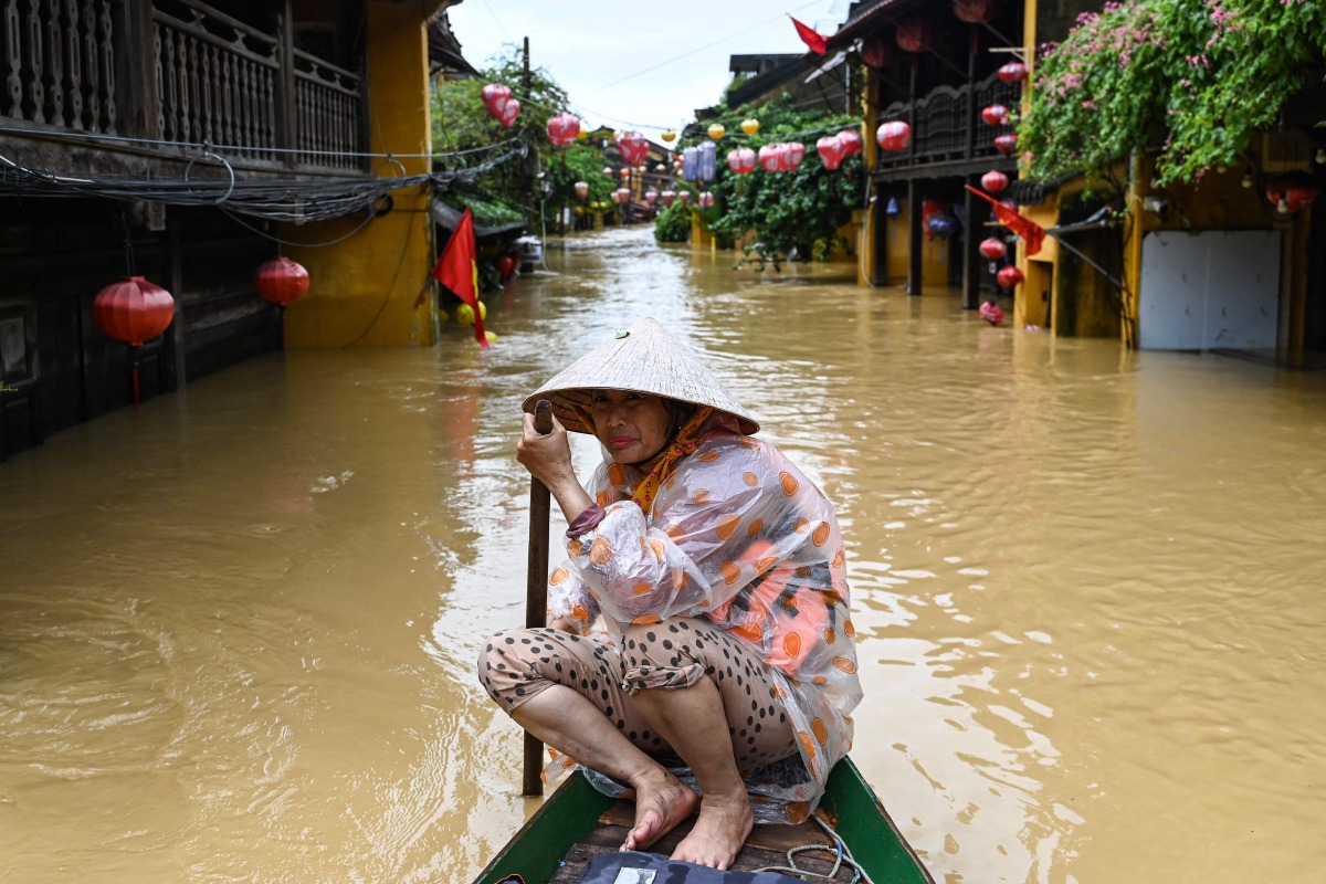 A woman rows a boat on a flooded street following heavy rains in Hoi An on October 30, 2025. (Photo by NHAC NGUYEN / AFP)