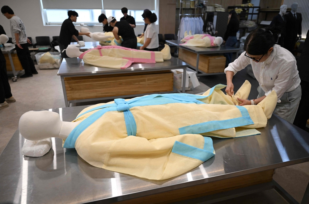 In a photo taken on September 24, 2025, students drape a mannequin in traditional Korean funeral cloth during a funeral administration class in Busan. (Photo by Jung Yeon-je / AFP)
