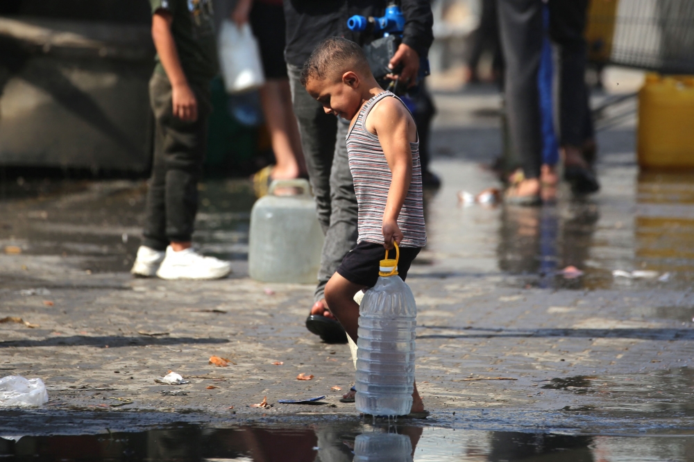 A Palestinian boy carries a large plastic bottle filled with water, after collecting it at a camp for displaced people in the Nuseirat refugee camp, located in the central Gaza Strip, on November 2, 2025. (Photo by Eyad Baba / AFP)
