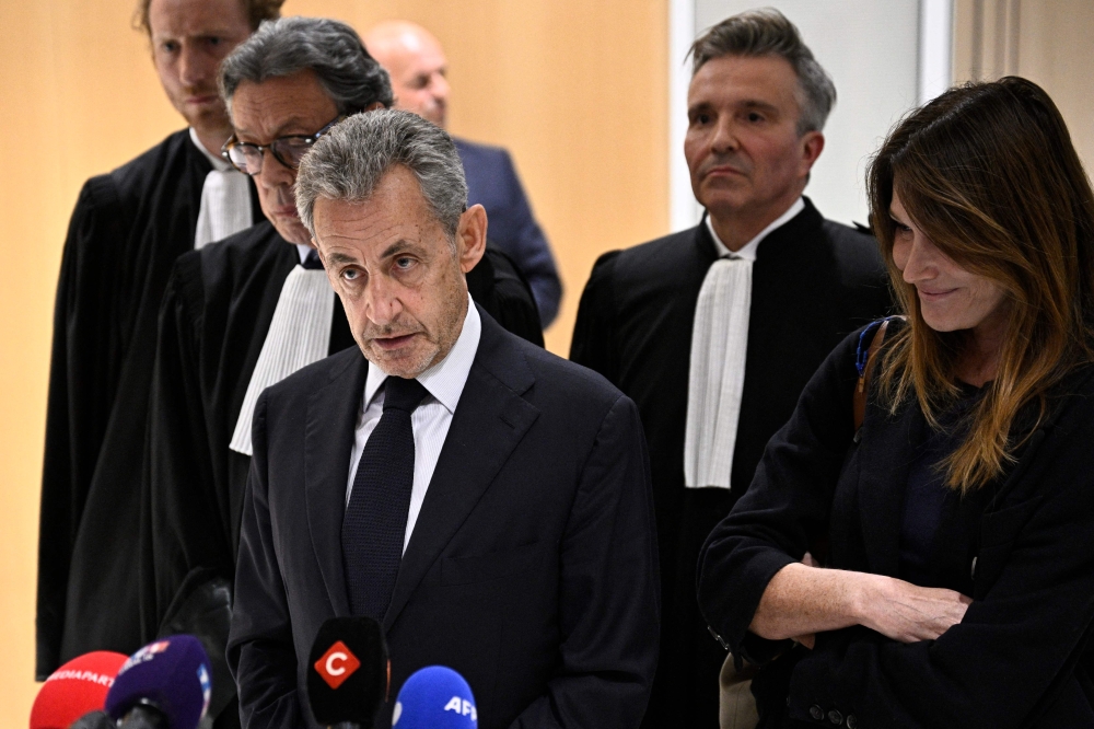 Former French president Nicolas Sarkozy speaks to the press flanked by his wife Carla Bruni and French lawyer Jean-Michel Darrois after the verdict in his trial at the Tribunal de Paris courthouse in Paris, on September 25, 2025. Photo by Julien De Rosa / AFP
