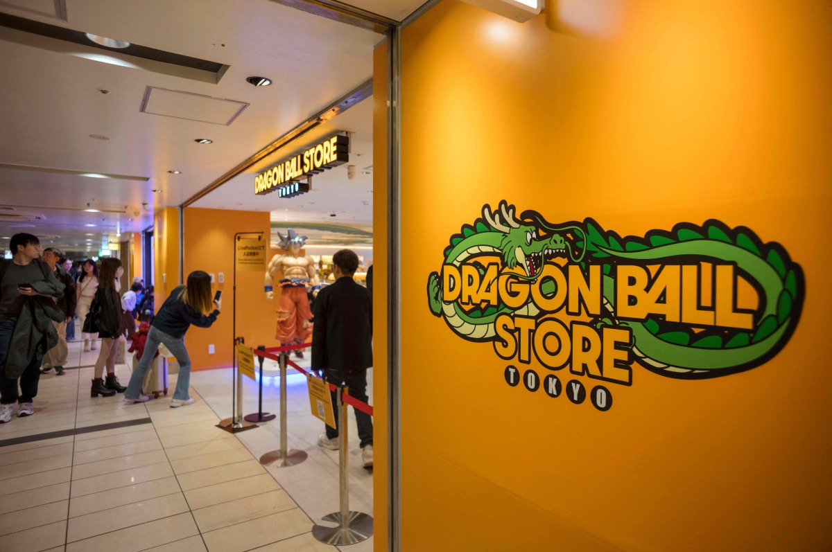 A passerby takes a photo next to a figurine of a manga character displayed in front of the Dragon Ball store at a shopping mall near Tokyo Station on November 14, 2025. (Photo by Kazuhiro NOGI / AFP)