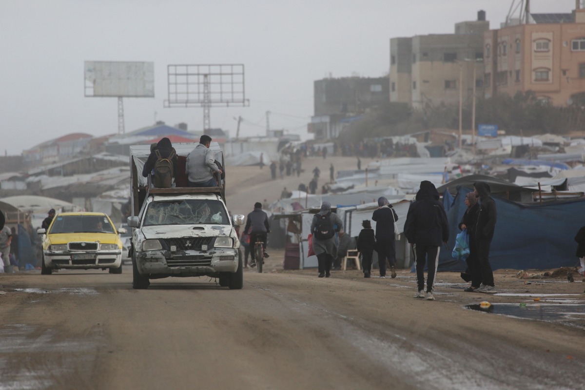 Displaced Palestinian walk past a vehicle carrying others west of Deir al-Balah city in the central Gaza Strip, on November 15, 2025 as a low-pressure system impacts the area. (Photo by Bashar TALEB / AFP)