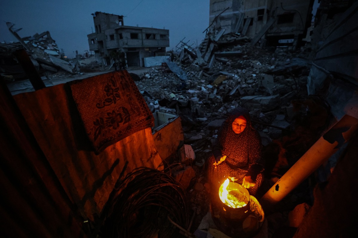 A displaced Palestinian woman warms herself beside a fire amid the ruins of destroyed buildings in the Bureij refugee camp, in the central Gaza Strip, on November 29, 2025. (Photo by Eyad Baba / AFP)
