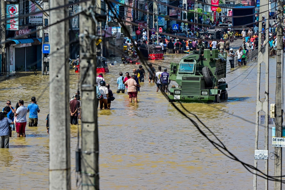 Damaged wires dangle from electric poles as an army truck wades through a flooded street after heavy rainfall in Wellampitiya on the outskirts of Colombo on November 30, 2025. (Photo by Ishara S. Kodikara / AFP)