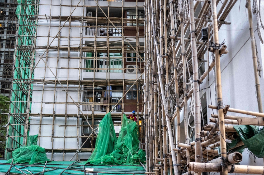 A construction worker removes the netting of bamboo scaffolding at Sui Wo Court housing estate in Fo Tan district of Hong Kong on December 4, 2025. (Photo by Philip Fong / AFP)