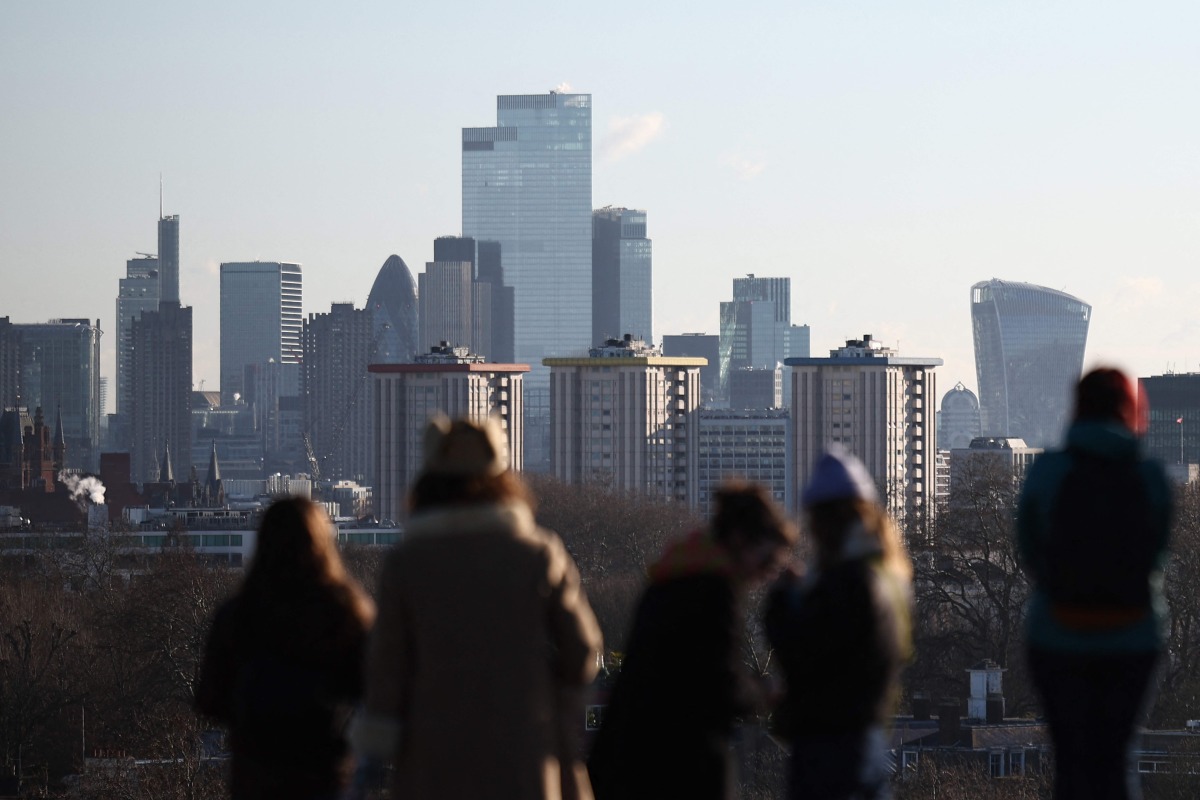 People look out at the view of the skyline of the financial office buildings in the City of London from Primrose Hill in London on January 2, 2026. Photo by HENRY NICHOLLS / AFP