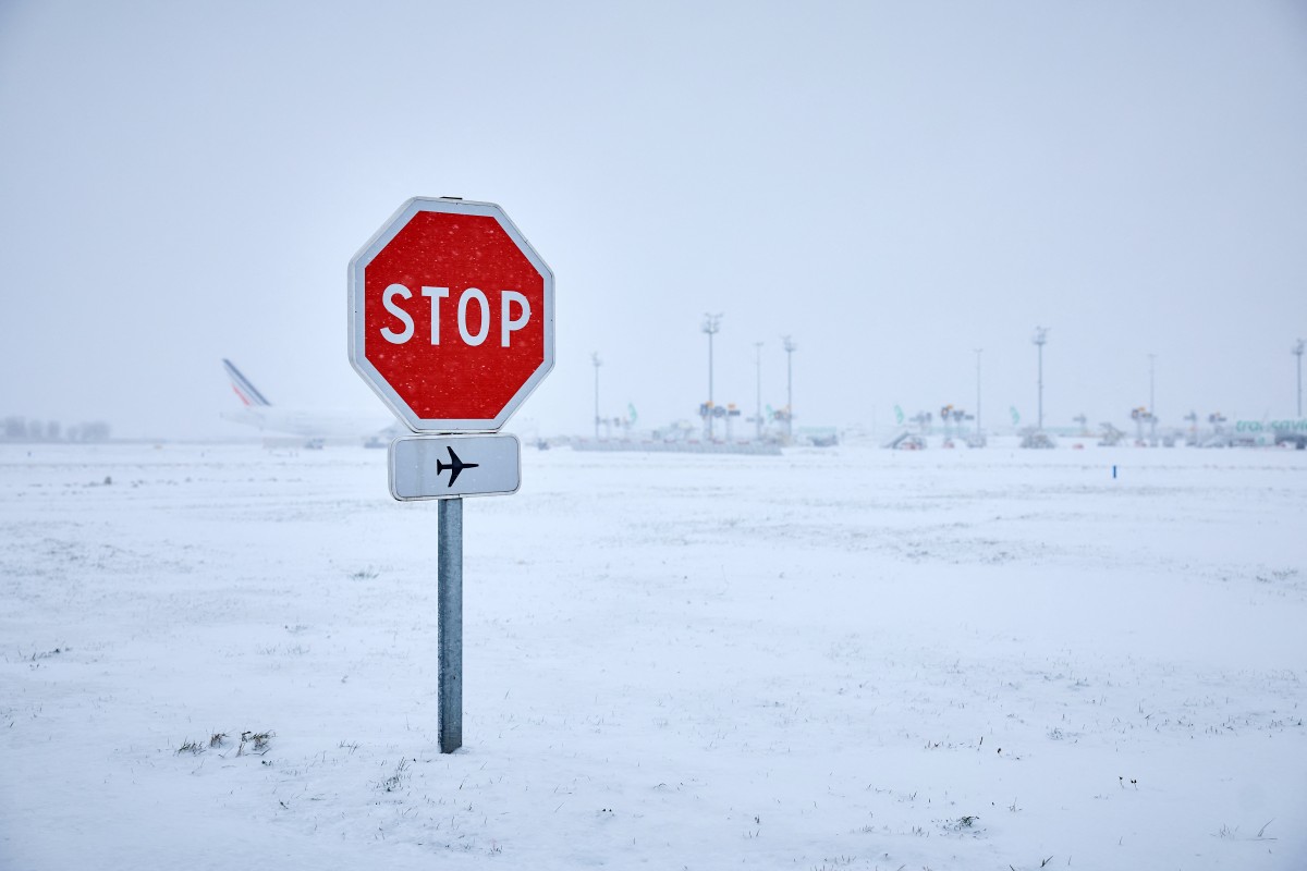 This photograph shows a stop sign near runways as snow blankets the tarmac, causing flight cancellations at Orly Airport, south of Paris on January 7, 2026. Photo by KIRAN RIDLEY / AFP