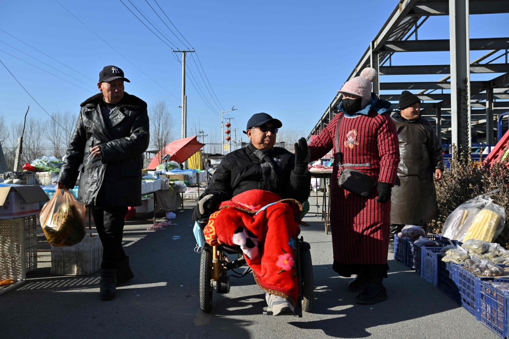 People in winter clothes trade at a traditional market in a neighbourhood affected by the heating subsidy policy, in Baoding city, northern China's Hebei province on January 7, 2026. (Photo by Adek Berry / AFP) 