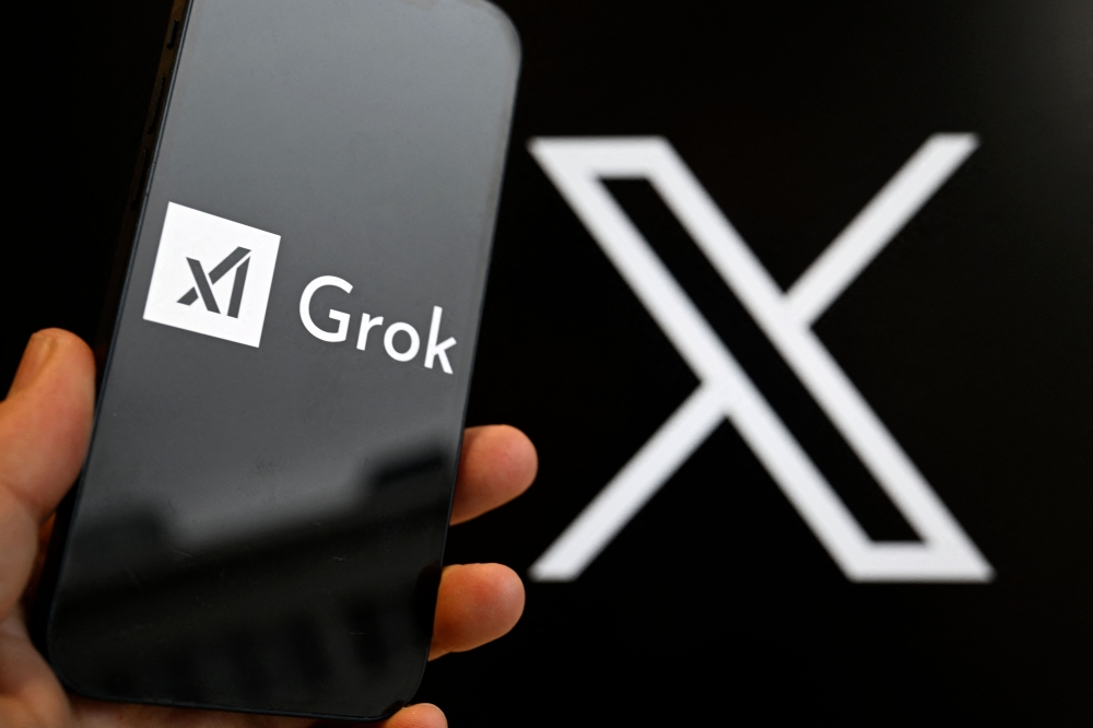 (Files) This photograph shows a smartphone bearing the logo of Grok in front of the X logo in Brussels on January 12, 2026. (Photo by Nicolas Tucat / AFP)