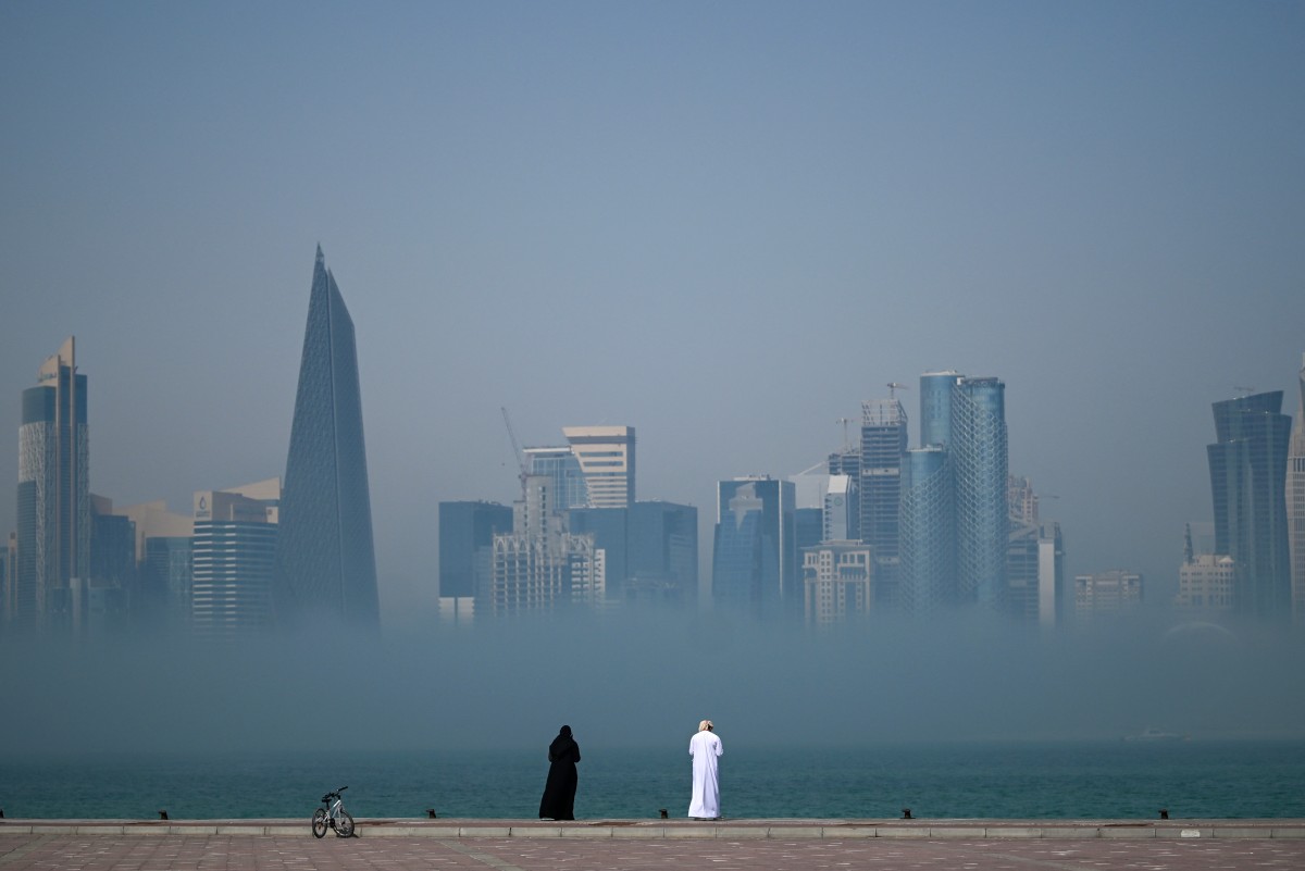 People look at the skyline covered in fog in Doha on February 9, 2026. (Photo by Mahmud HAMS / AFP)
