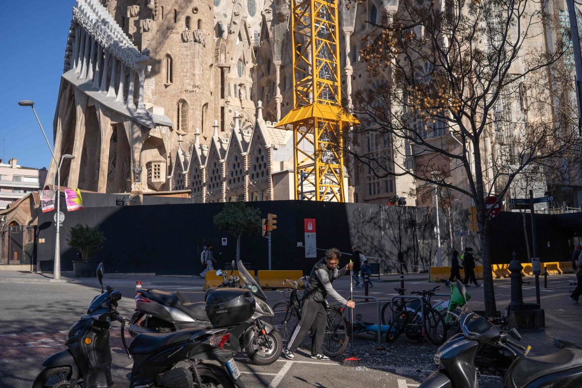 A man cleans broken glass on the floor next to Sagrada Familia Basilica amid a strong wind alert due to Storm Nils in Barcelona, on February 12, 2026. (Photo by Manaure QUINTERO / AFP)