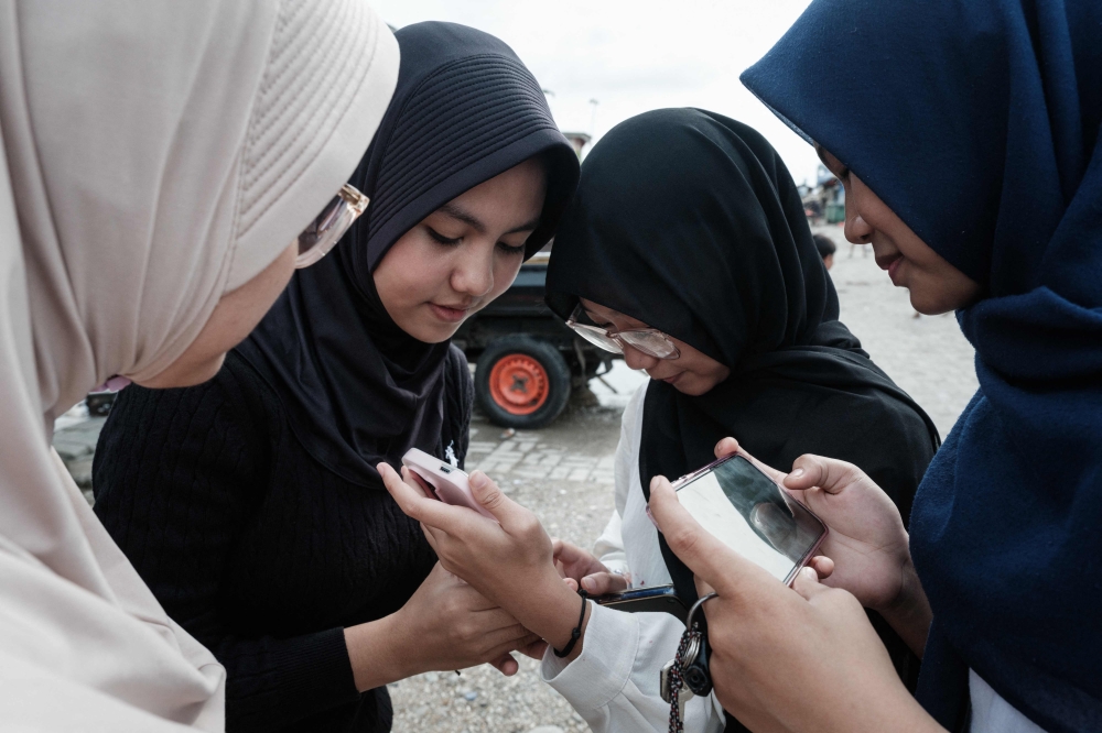 15-year-old girls use their smartphones on a street in Jakarta on March 26, 2026. (Photo by Yasuyoshi Chiba / AFP) 