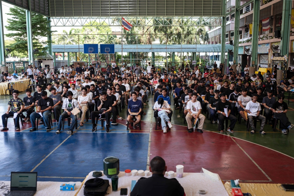 A group of men wait for the drawing of the Thai military conscription lottery at Watmatchantikaram School in Bangkok on April 7, 2026. (Photo by Chanakarn Laosarakham / AFP)