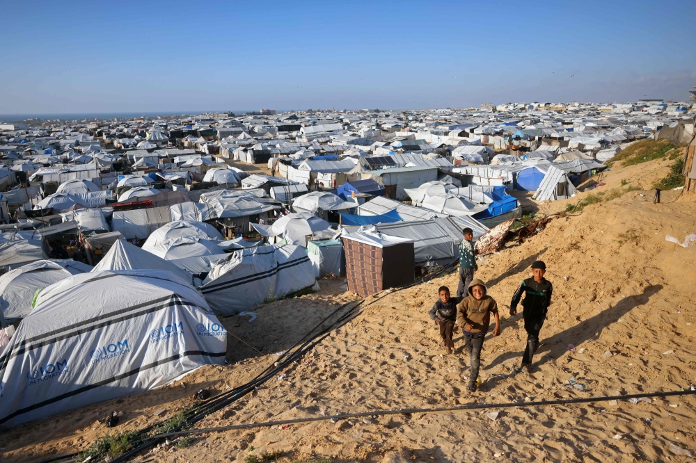 Boys walk past the tents at a makeshift camp for displaced Palestinians in Khan Yunis, in the southern Gaza Strip on April 10, 2026. (Photo by Bashar Taleb / AFP)