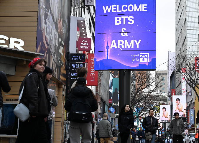 Tourists walk past a “Welcome BTS” sign in Myeong-dong, central Seoul, on Friday, a day ahead of the group’s comeback concert. (Lee Sang-sub/The Korea Herald)
