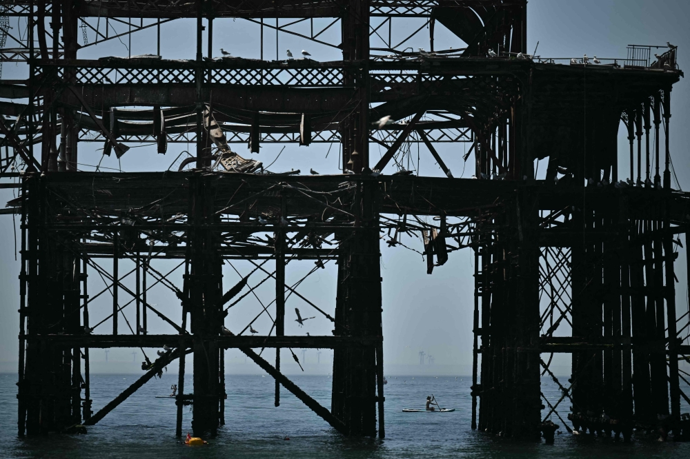 A paddleboarder is seen between the stanchions of the derelict West Pier off the beach in Brighton, on the south coast of England on May 25, 2026, as Monday is expected to be the hottest bank holiday.(Photo by Ben Stansaal / AFP)
 