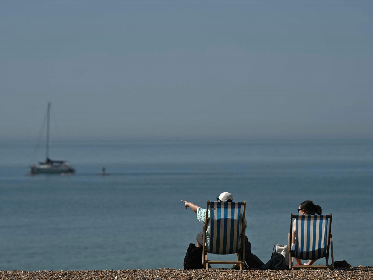People relax in deck chairs on the beach in Brighton, on the south coast of England on May 25, 2026, as Monday is expected to be the hottest bank holiday ever, with heatwave conditions spreading to parts of southeast England and London. (Photo by Ben STANSALL / AFP)