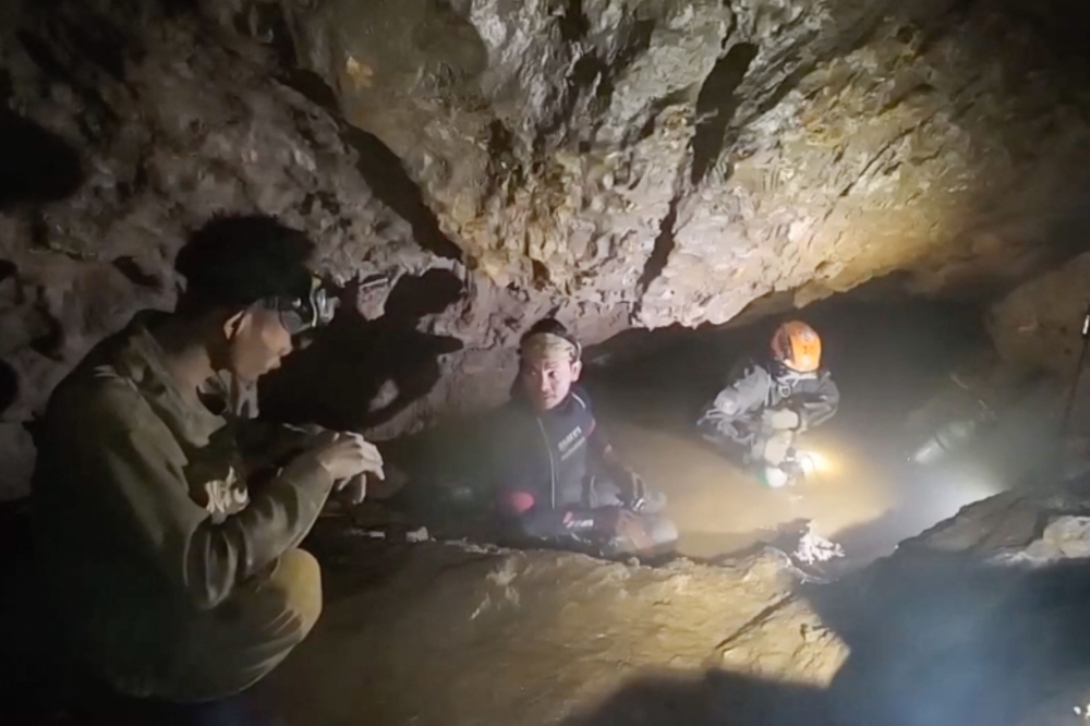 This screengrab made from handout video footage taken on May 29, 2026, shows a rescue team (C, R) about to free one (L) of seven men trapped in a semi-submerged cave. (Photo by Handout / Benz Norrased Palasing / Seascout Diving / AFP) 