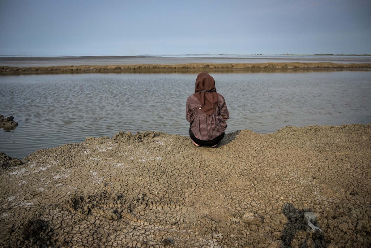 A resident affected by the Lapindo mudflow sits on the embankment in the mud volcano area, marking 20 years since a gas exploration accident triggered a mud flow that inundated more than a dozen villages and permanently displaced tens of thousands of people in Porong, Sidoarjo, East Java province on May 29, 2026. (Photo by JUNI KRISWANTO / AFP)