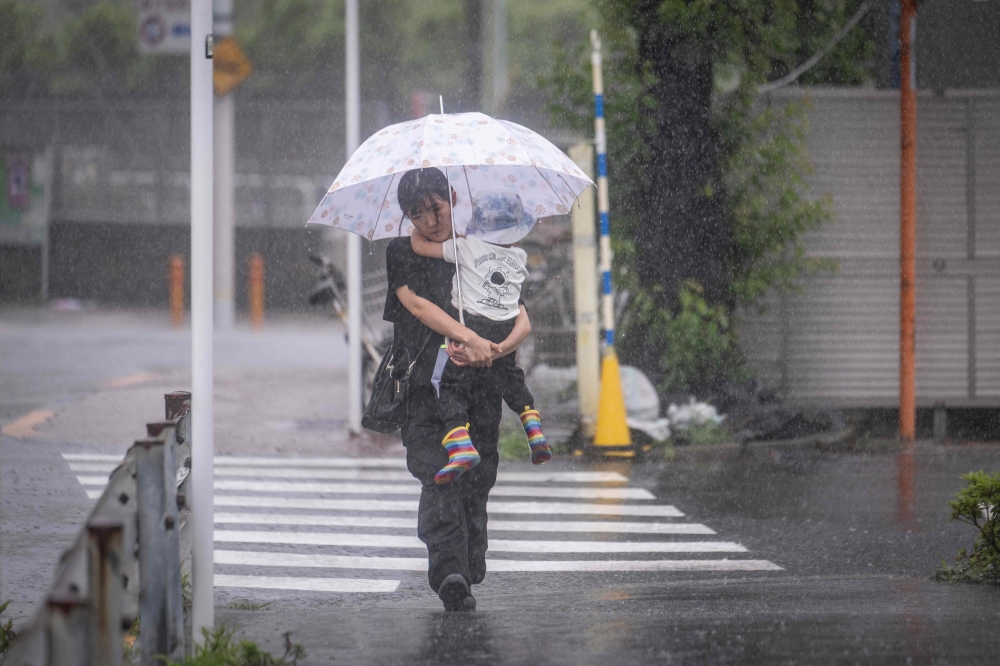 A woman holding her child walks through heavy rain brought by severe tropical storm Jangmi in Tokyo on June 3, 2026. (Photo by Yuichi Yamazaki / AFP)