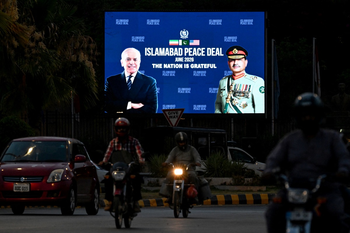 Commuters ride past an electronic board featuring Pakistan's Prime Minister Shehbaz Sharif (L) with Army Chief and Field Marshal Syed Asim Munir, displayed along a road in Islamabad on June 18, 2026 after the US–Iran peace deal announcement. Photo by Aamir Qureshi / AFP