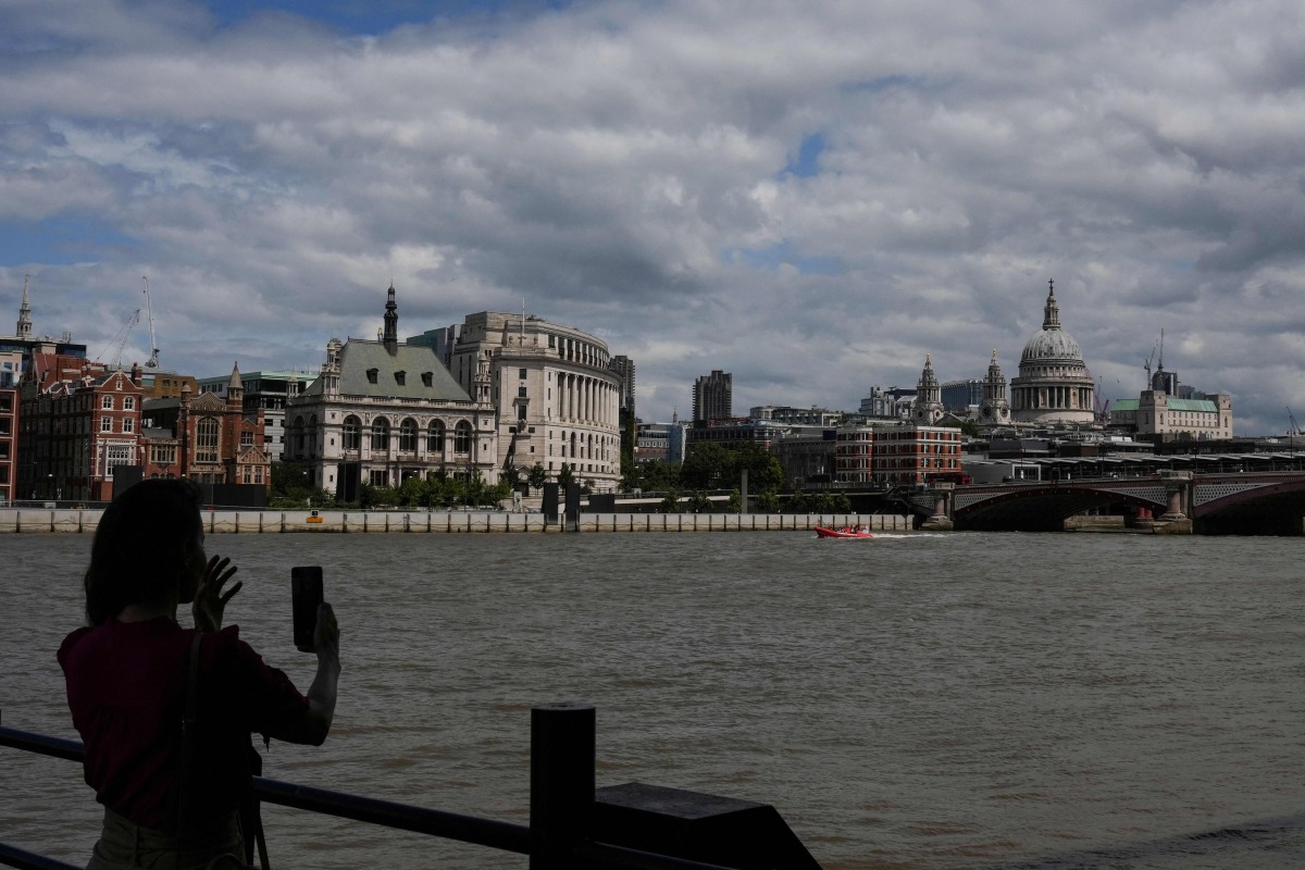 A woman takes a photo toward St. Paul's from the south side of the River Thames in central London on June 28, 2026, as people come out to take advantage of cooler temperatures following days of extreme heat. The UK broke the record for a June temperature for the third day in a row on June 26, the Met Office weather agency said, as a sweltering heatwave strained schools and hospitals and drove down business. (Photo by CARLOS JASSO / AFP)
